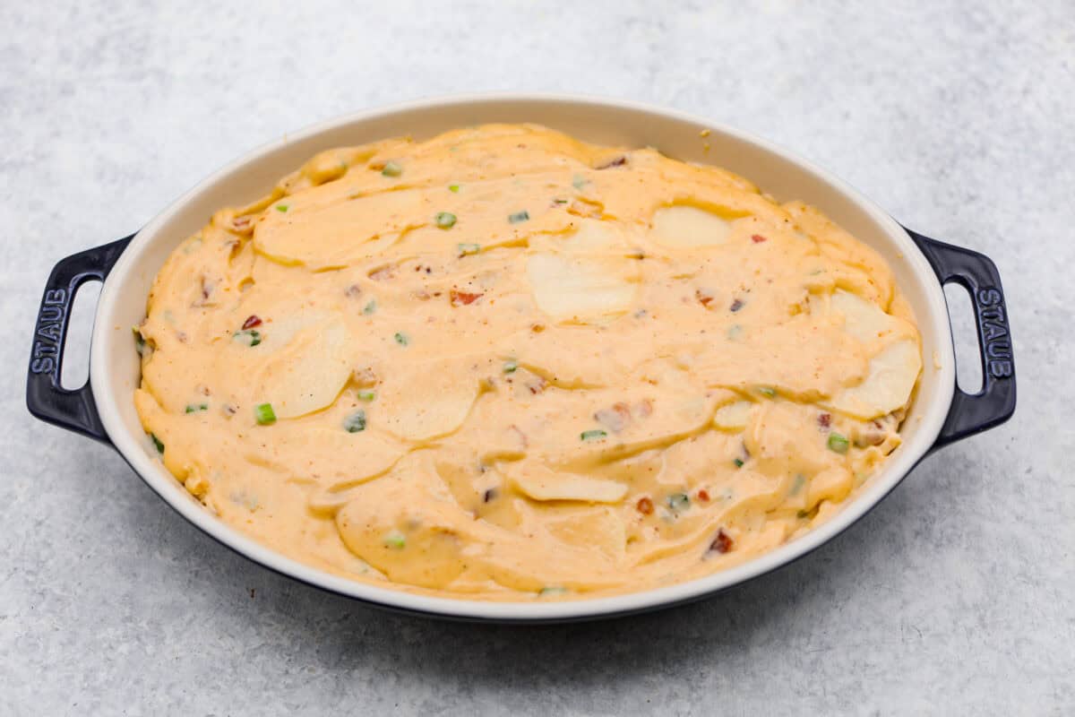 Overhead shot of the potatoes and sauce spread into a baking dish. 