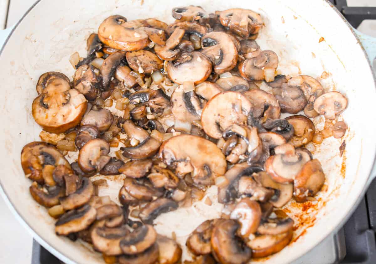 overhead shot of mushrooms cooking in garlic in a skillet. 