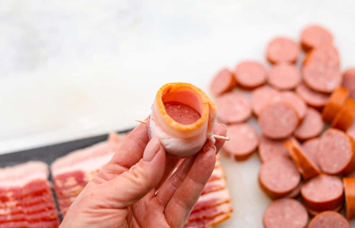 Angle shot of a sausage slice wrapped in bacon with a toothpick sticking through it. 