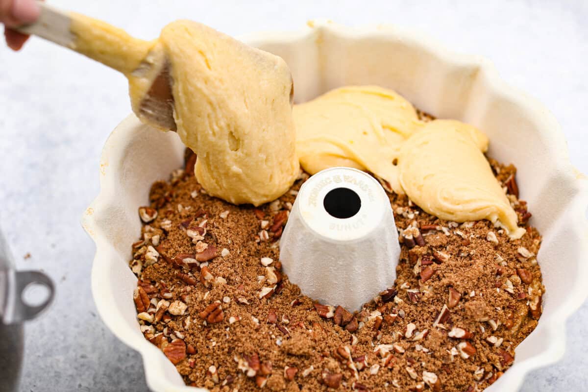 This Sock It to Me Cake is a moist, buttery Southern bundt cake with a delicious cinnamon-sugar pecan layer swirled through the middle. It became popular because of Duncan Hines in the 1960s and 1970s, and you'll understand why once you try it! Overhead shot of someone scooping the rest of the cake batter over the filling in the bundt pan.
