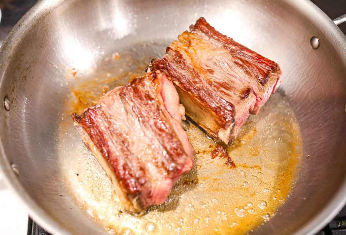 Overhead shot of short ribs searing in a skillet. 