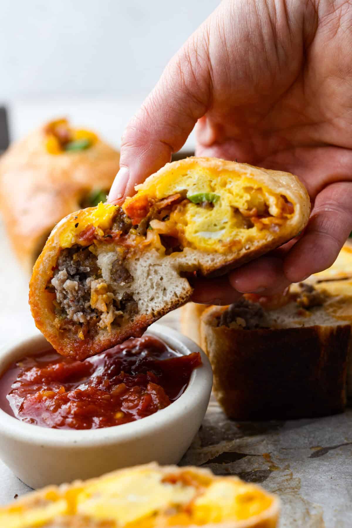 Side shot of someone dipping a piece of the breakfast Stromboli into salsa. 