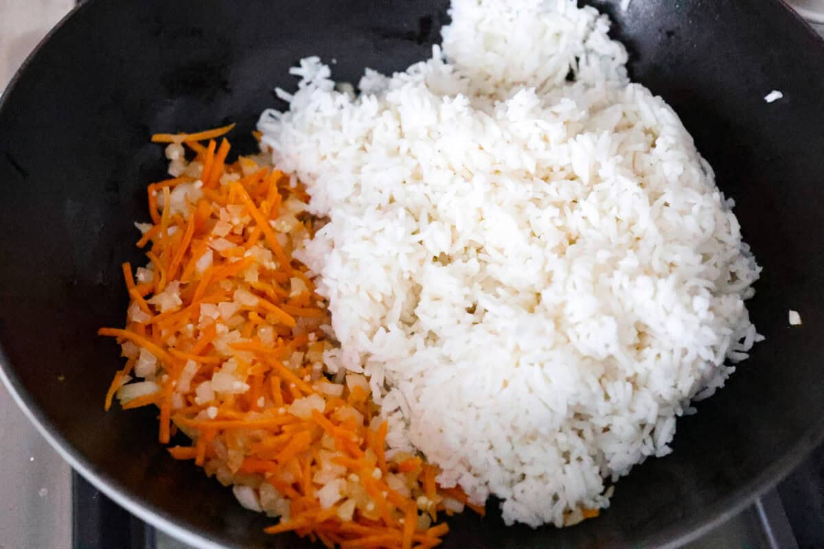 Overhead shot of cooked rice being added to the cooked vegetables in the skillet. 