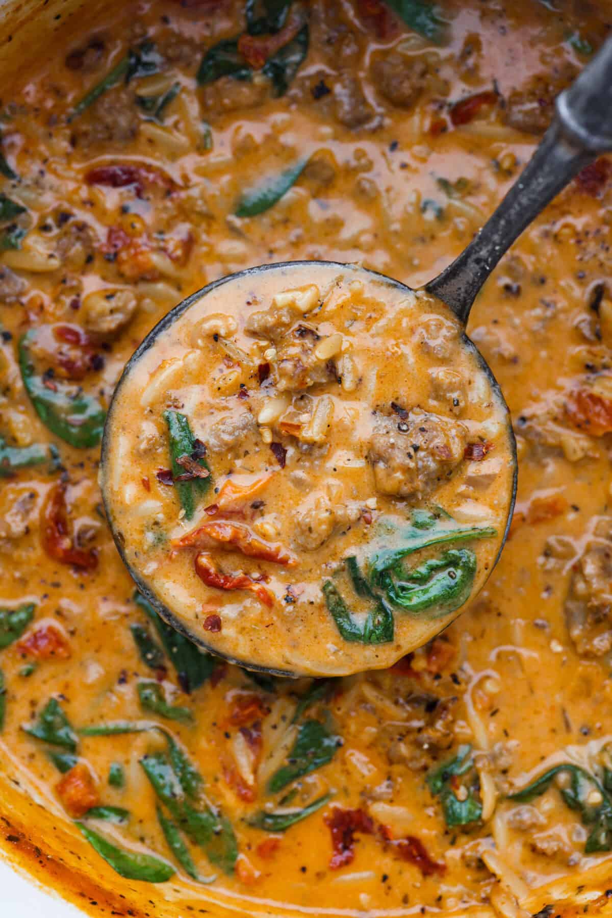 Close up shot of marry me sausage orzo soup in a ladle over the pot of soup.