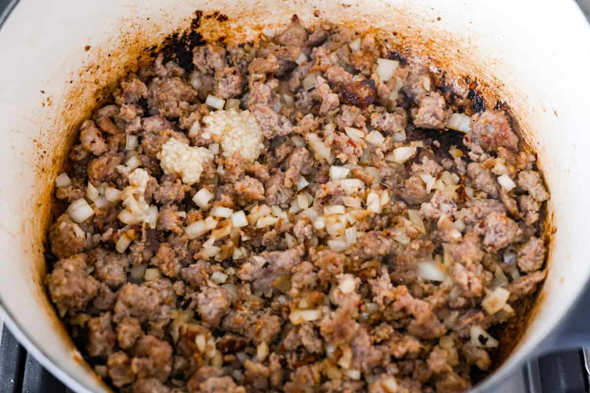 Overhead shot of sausage and onions cooking in a pot. 