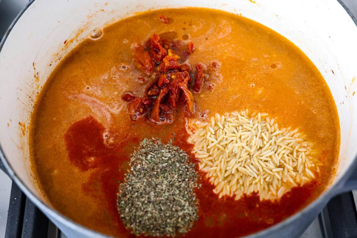 Overhead shot of chicken broth, seasonings, orzo and sun dried tomatoes added to the sausage and onions. 