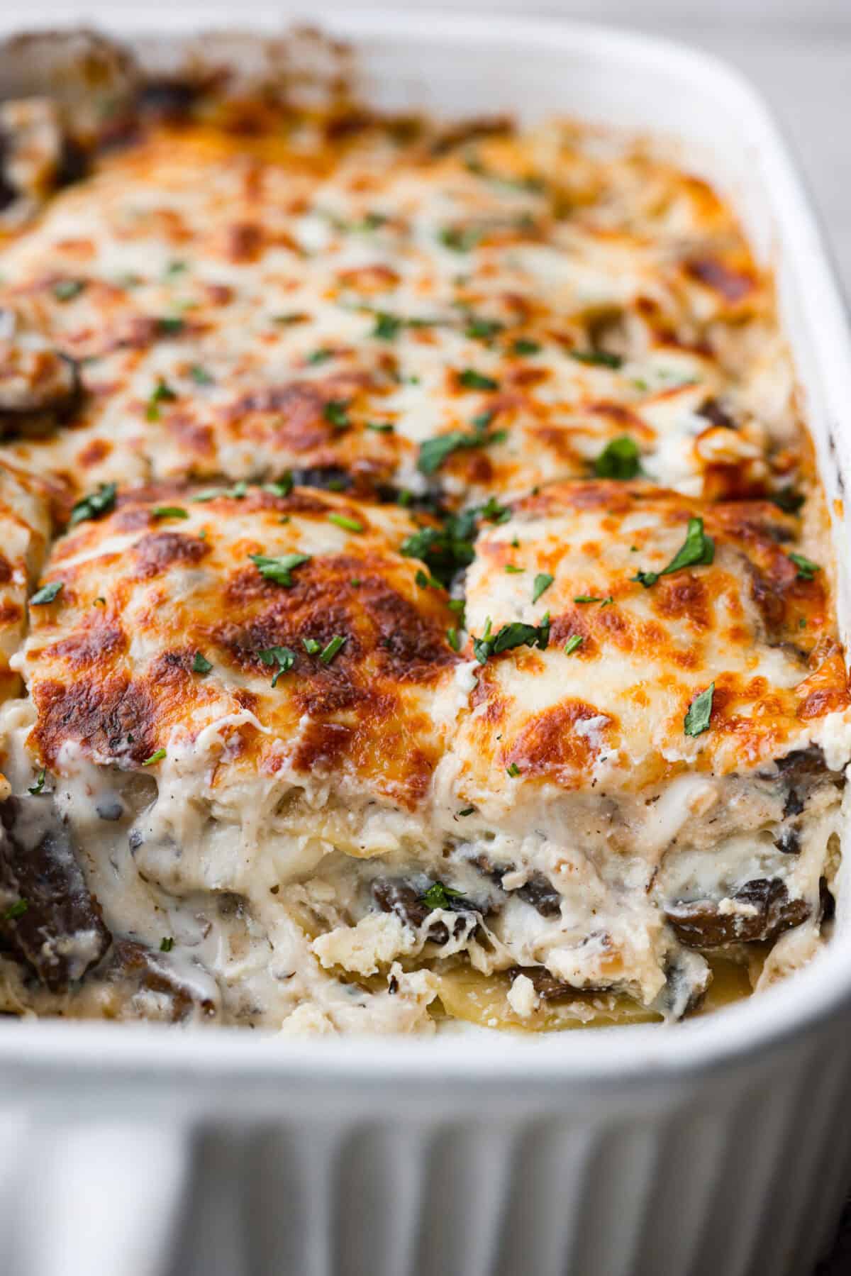 Close up shot of mushroom lasagna in a baking dish with slices taken out. 