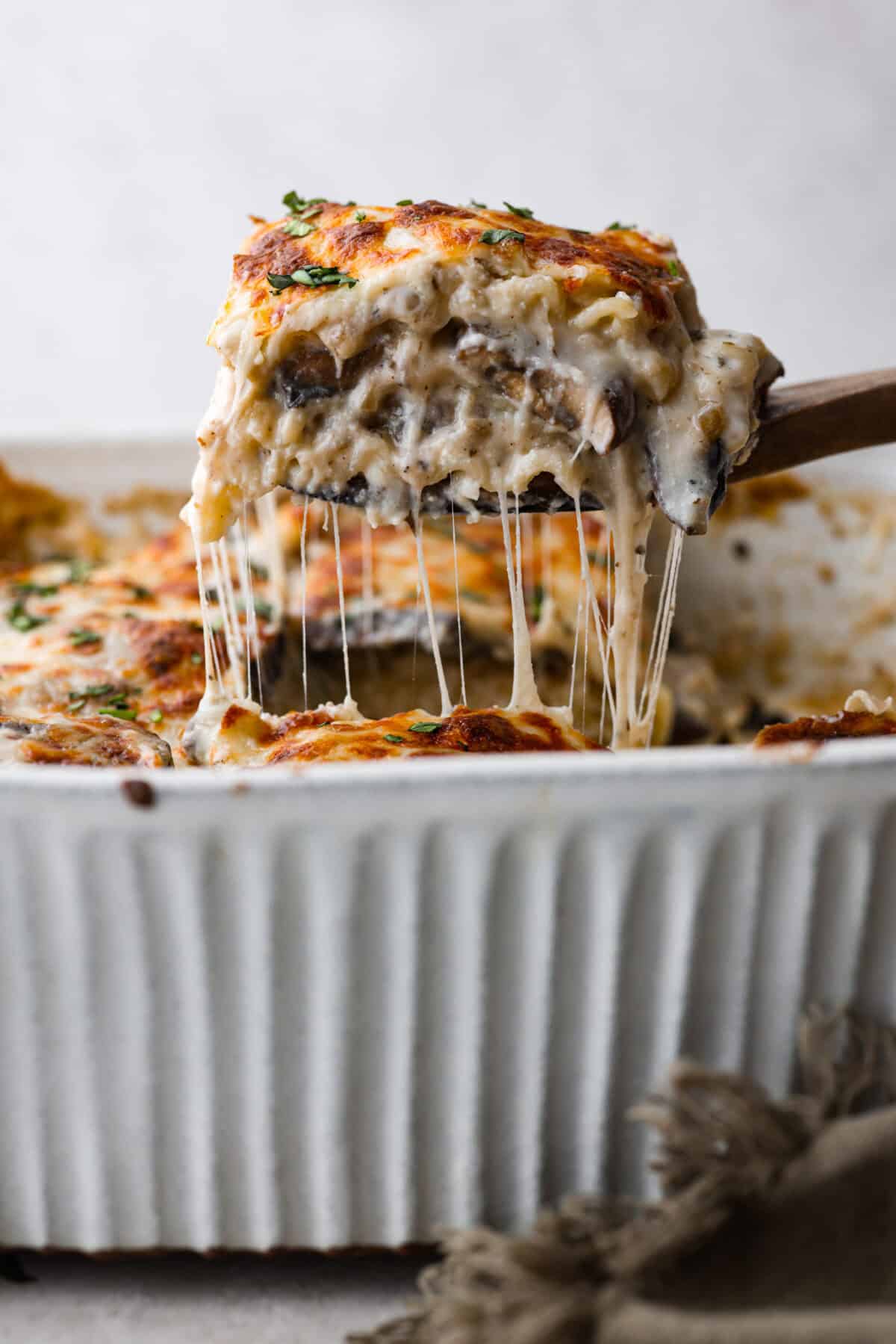 Side shot of a piece of mushroom lasagna being lifted out of the baking dish with a wooden spatula. 