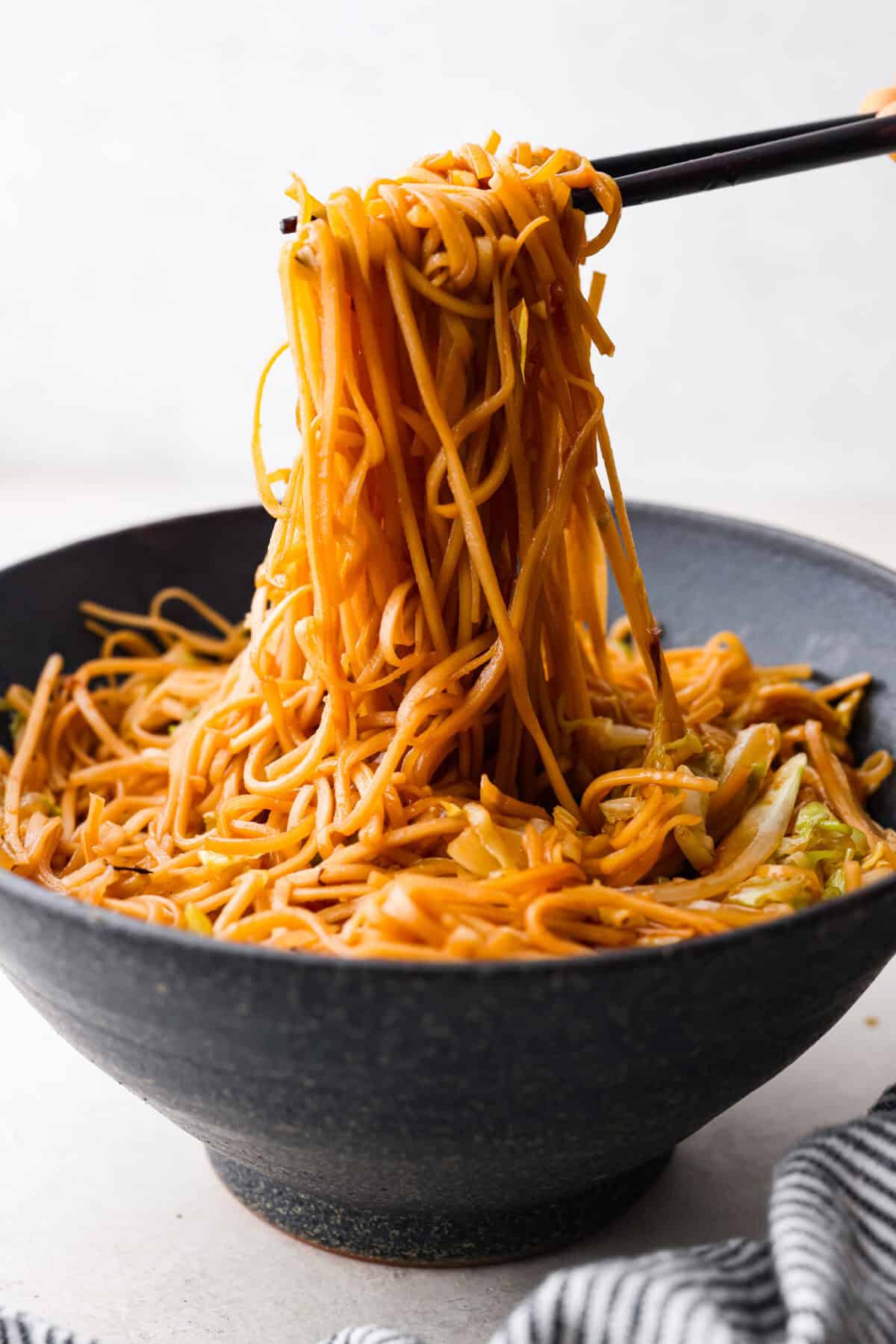 Side shot of chopsticks pulling up a large bite of panda express low mein noodles from a bowl. 