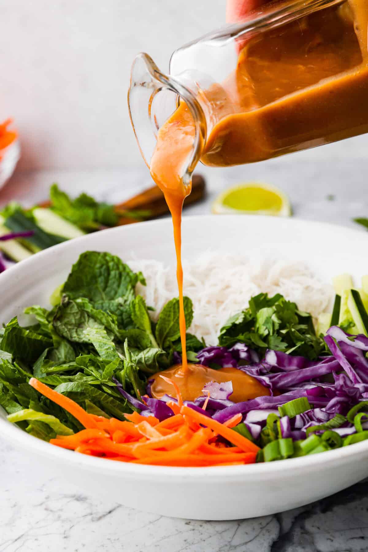 Side shot of someone pouring Thai peanut dressing into the spring roll bowl.