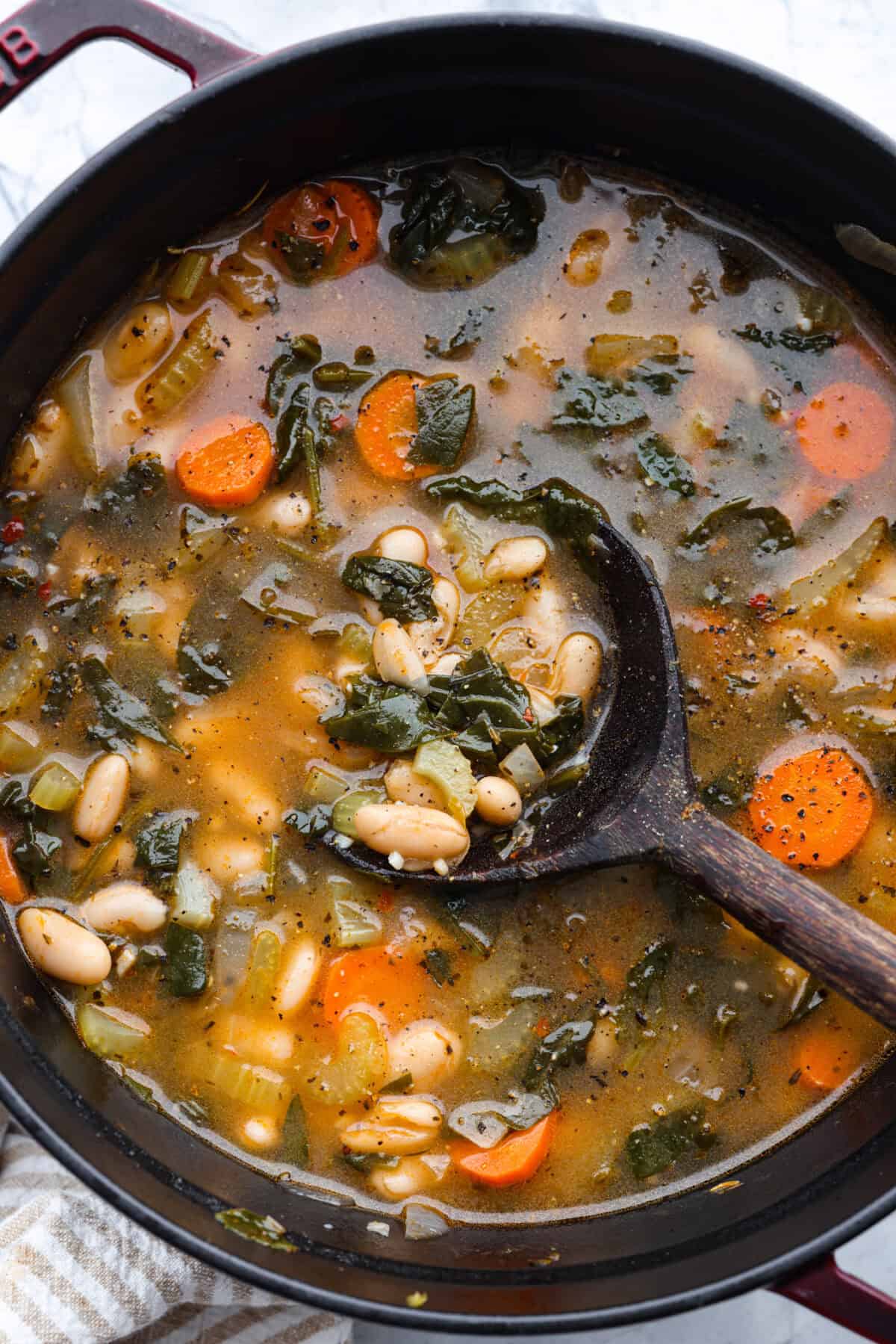 Overhead shot of Tuscan white bean soup in a pot with a wooden spoon.