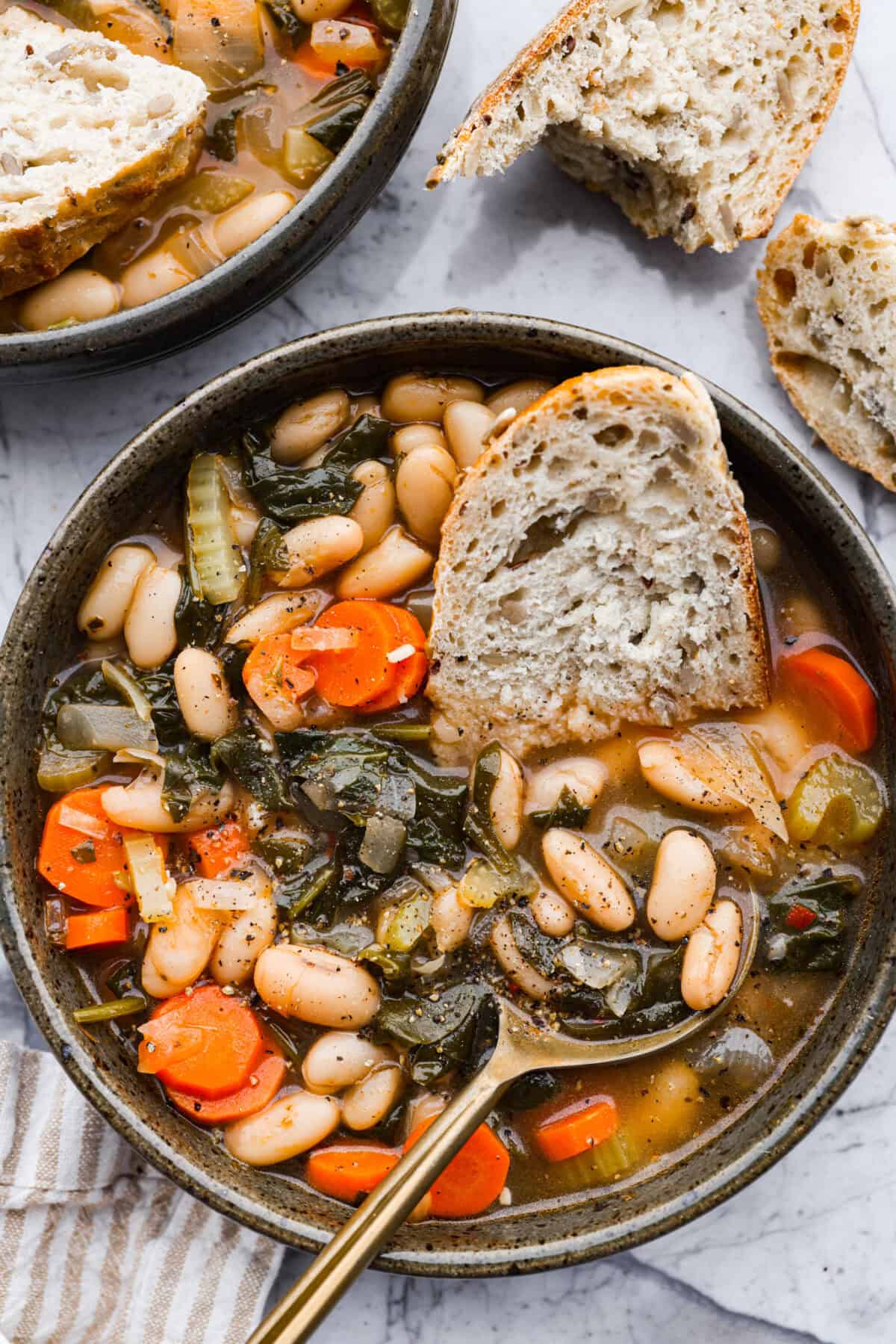 Overhead shot of a bowl of Tuscan white bean soup with half a bun.