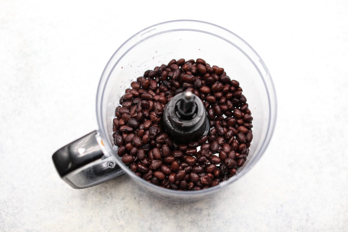 Overhead shot of black beans in a food processor. 