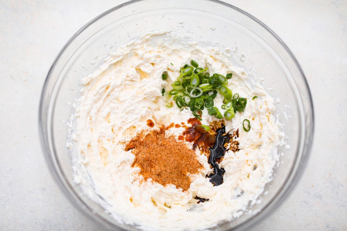 Overhead shot of green onion, lemon juice, seasonings, hot sauce and Worcestershire sauce on top of the cream cheese mixture. 