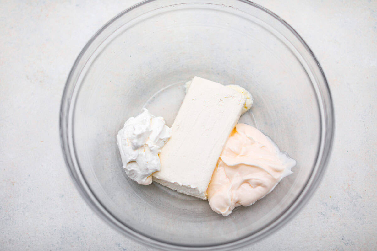 Overhead shot of softened cream cheese, mayo and sour cream in a mixing bowl. 