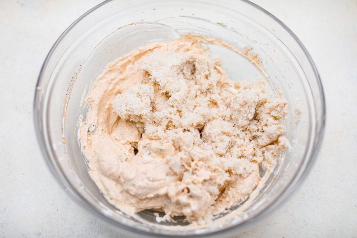 Overhead shot of crab meat added to the cream cheese and seasoning mixture in a mixing bowl.