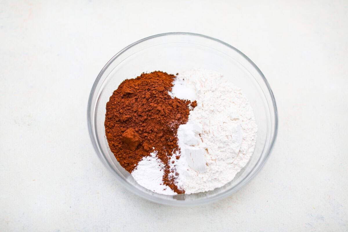 These double chocolate muffins are rich, moist, and packed with deep chocolate flavor! They are the perfect treat for breakfast, snack time, or dessert. They come together with simple ingredients and bake up beautifully with a soft, tender crumb in less than an hour! Mixing bowl with flour, baking soda, baking powder, salt and cocoa powder in a mixing bowl.