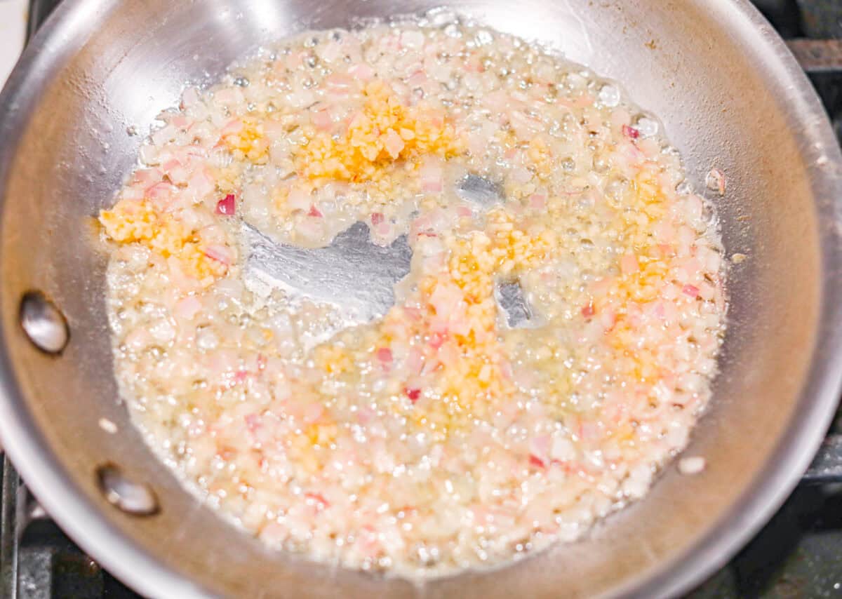 Overhead shot of garlic and shallots cooking in butter in a skillet. 