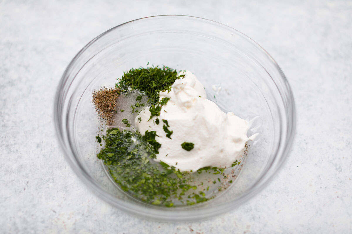 Overhead shot of sour cream. dill, parsley, salt, pepper, vinegar and sugar in a mixing bowl. 