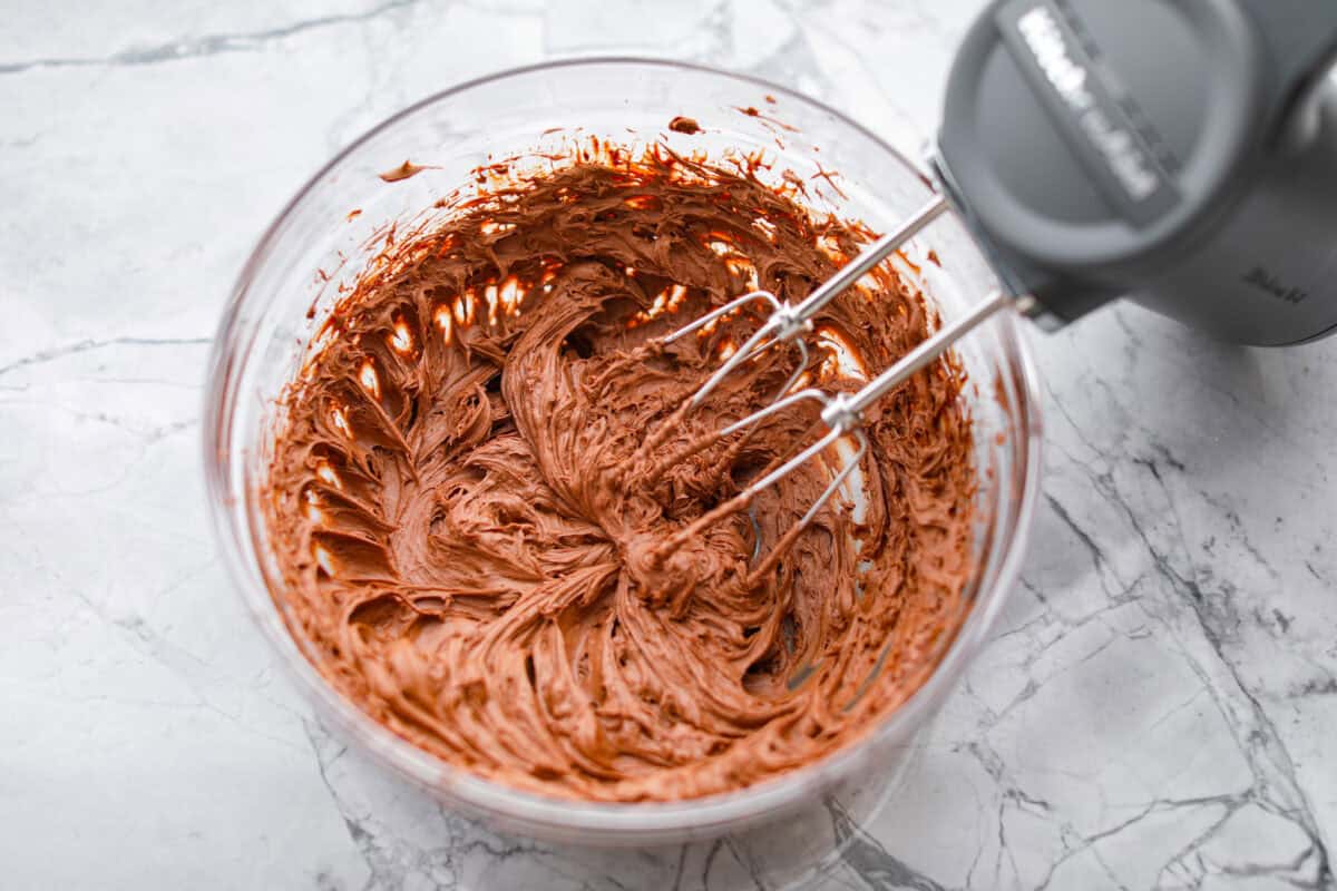 Overhead shot of someone using a hand mixer to whip up the chocolate chip mixture to make a fluffy ganache. 