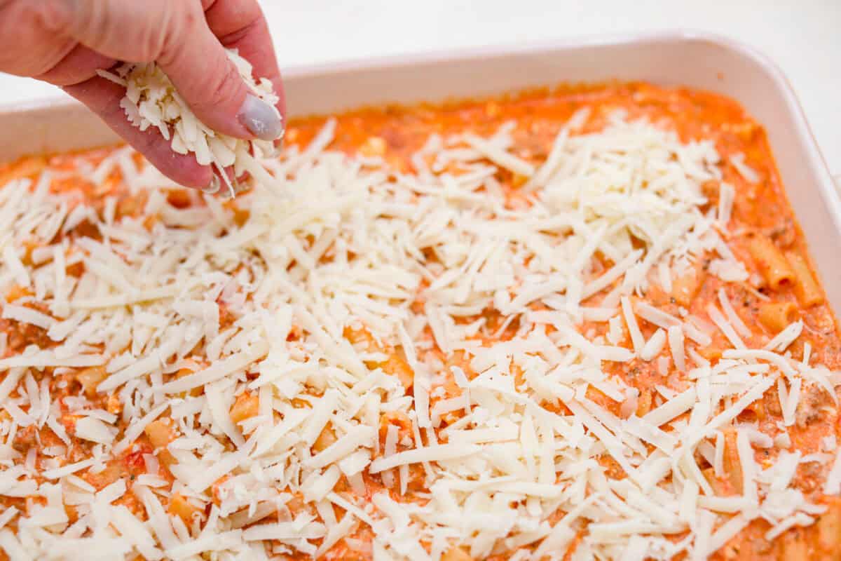 Angle shot of someone sprinkling cheese on top of the millioin dollar baked ziti casserole. 