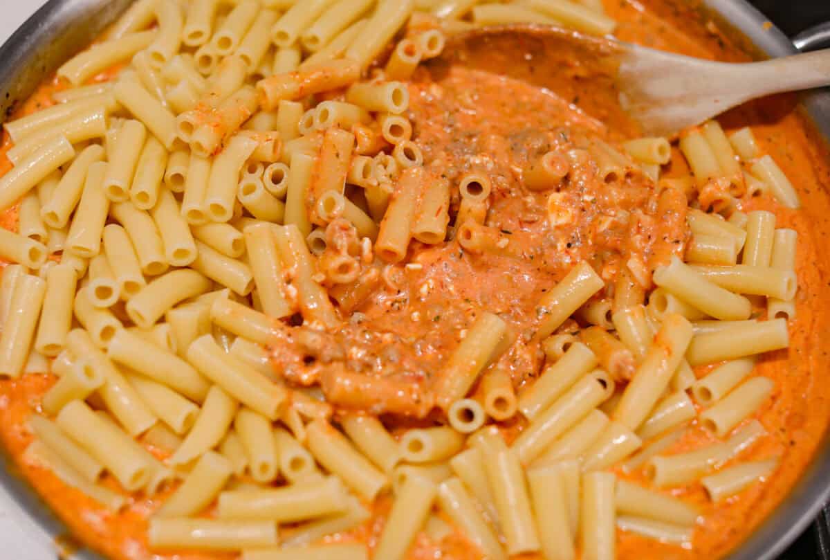 Overhead shot of ziti noodles being mixed in with the sauce. 