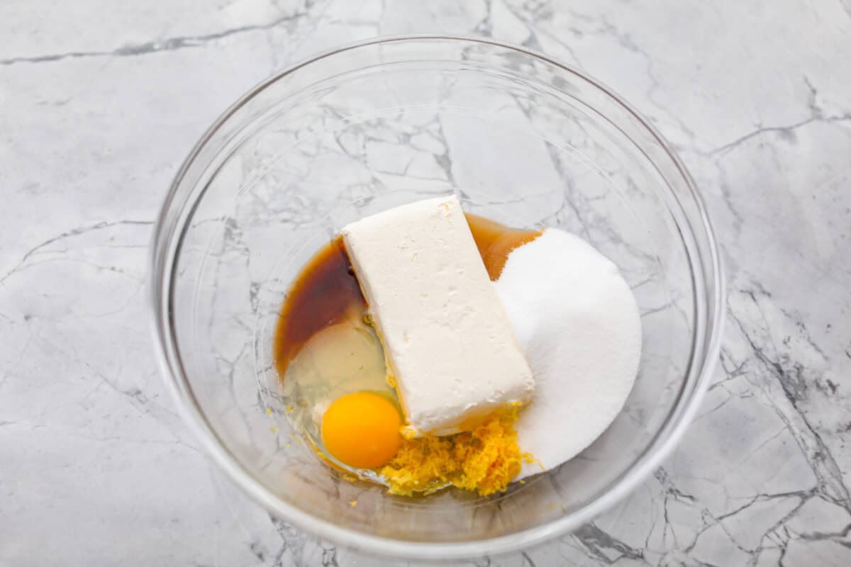 Overhead shot of cream cheese, egg, lemon zest, sugar and vanilla extract in a mixing bowl. 