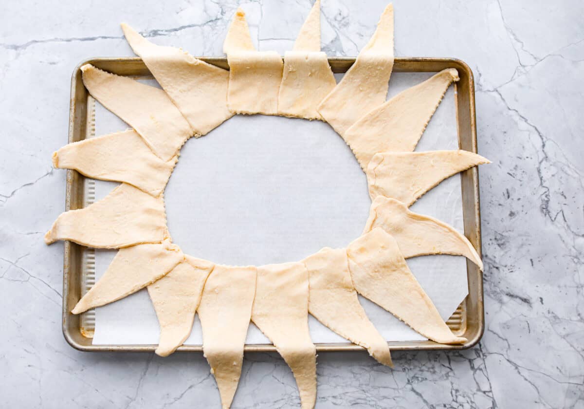 Overhead shot of a baking sheet with parchment paper and crescent rolls spread out in a sunburst shape. 