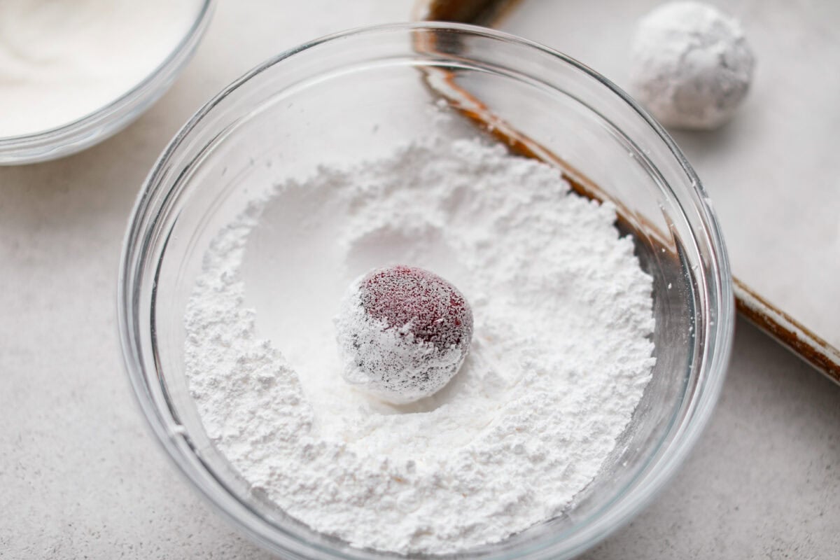 A cookie dough ball in a bowl of powered sugar.