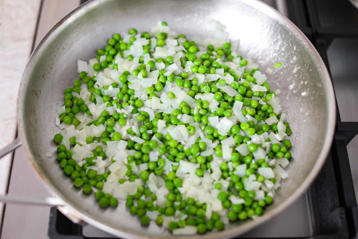 Overhead shot of garlic, onion, and peas sautéing in a pan. 