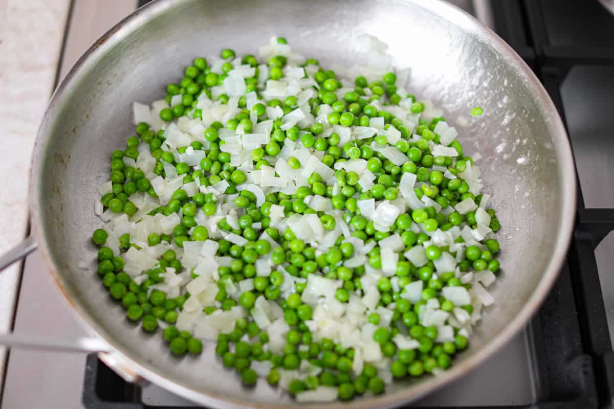 Stanley Tucci pasta casserole is everything you want in a casserole. It's simple to make and incredibly flavorful! TikTok is going crazy over the crispy bacon, tender peas, and the creamy, cheesy sauce that holds everything together! Overhead shot of garlic, onion, and peas sautéing in a pan.