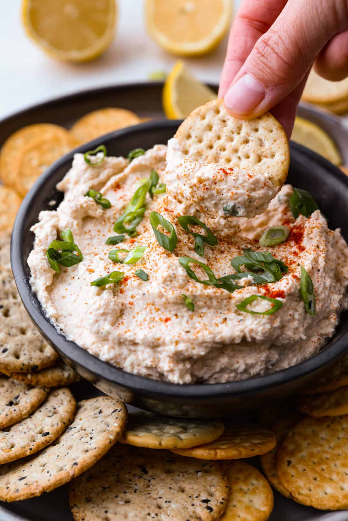 Angle shot of someone dipping a cracker into the cajun crab dip. 