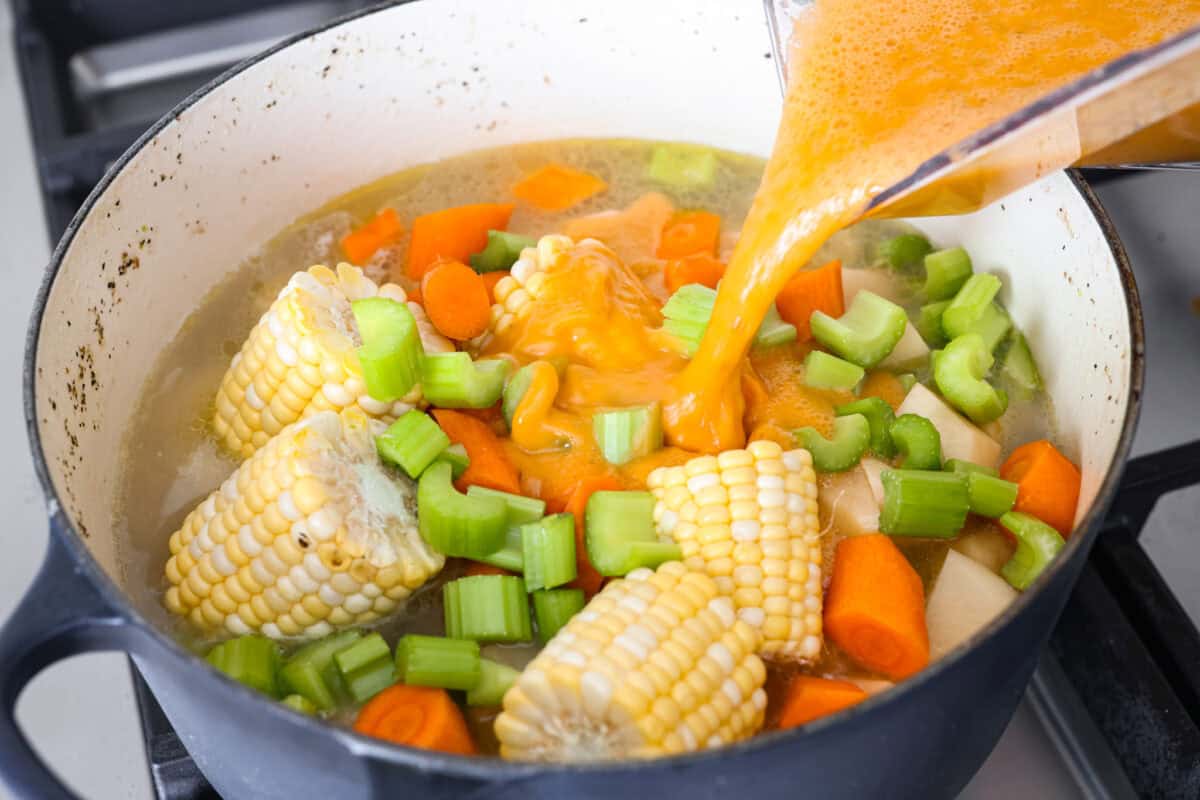 Angle shot of someone pouring blended ingredients back into the pot with other vegetables. 