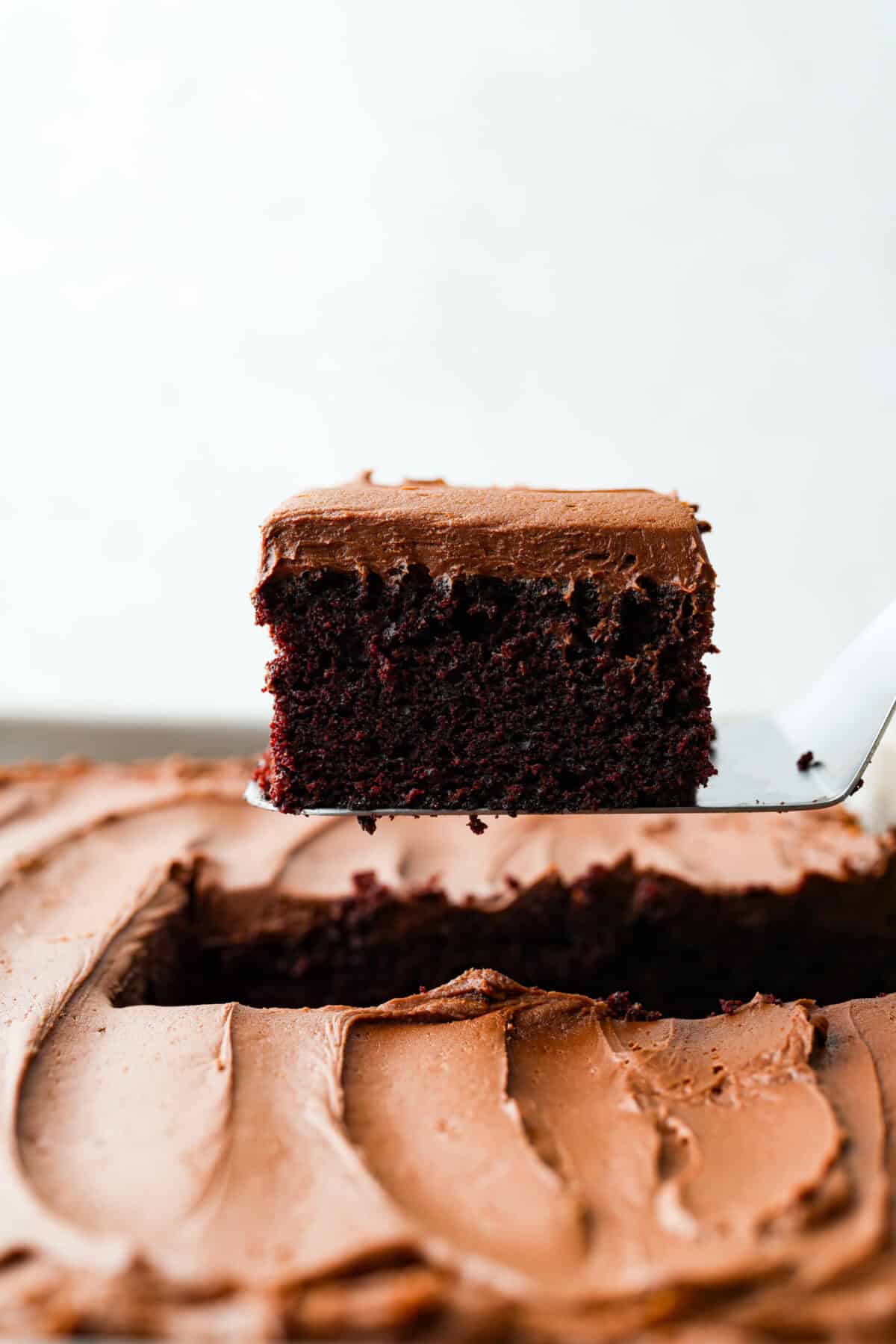 Side shot of a piece of cake being lifted out of the chocolate mayonnaise cake on a spatula. 