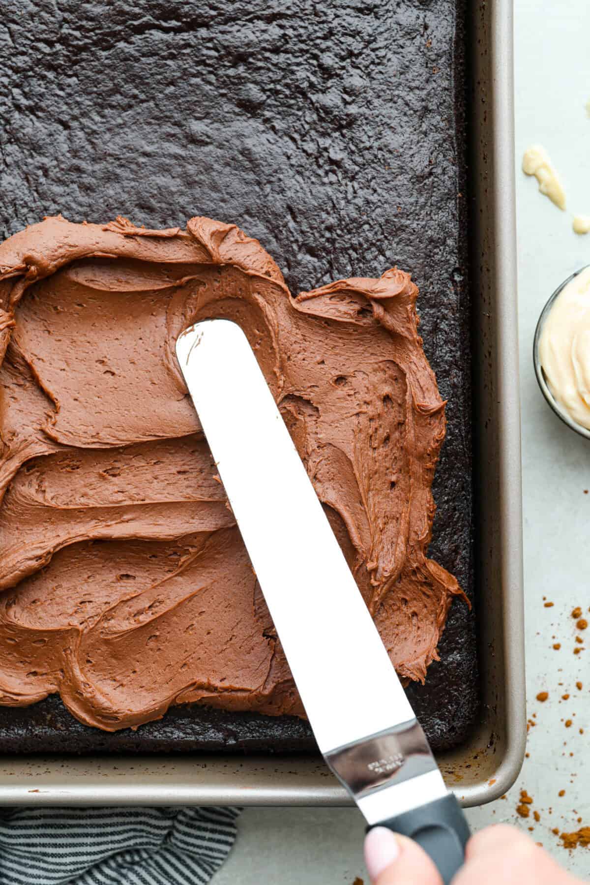 Overhead shot of someone frosting the chocolate mayonnaise cake with chocolate buttercream frosting. 