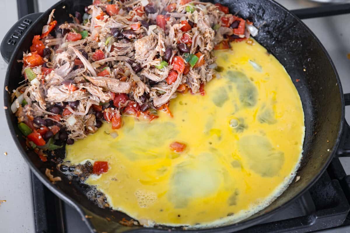 Overhead shot of pork mixture pushed to the side in a skillet with eggs cooking next to it.