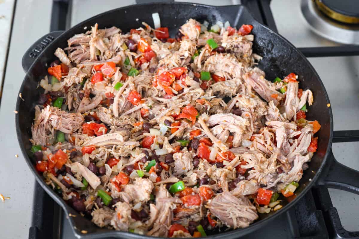 Overhead shot of pork, beans, and diced tomatoes added in to the cooked vegetables. 