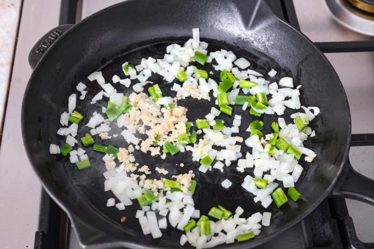 Overhead shot of onion, jalapeno, and garlic cooking in olive oil in in a skillet. 