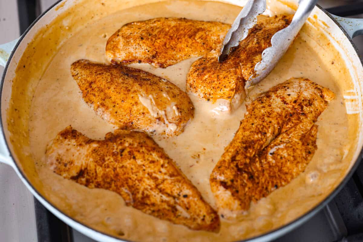 Close up shot of the chicken being added back into the creamy cajun sauce. 