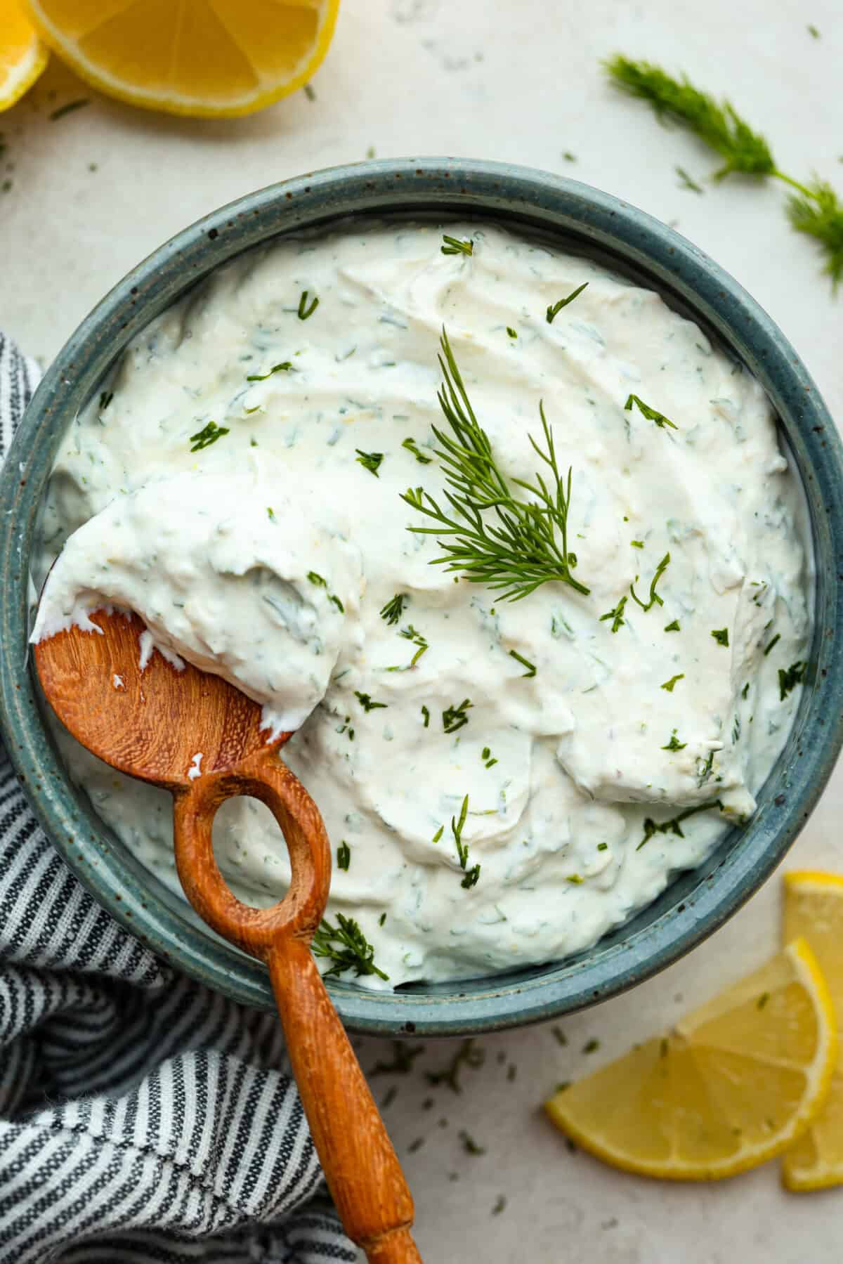 Overhead image of lemon dill sauce in a small serving bowl with wooden spoon. 