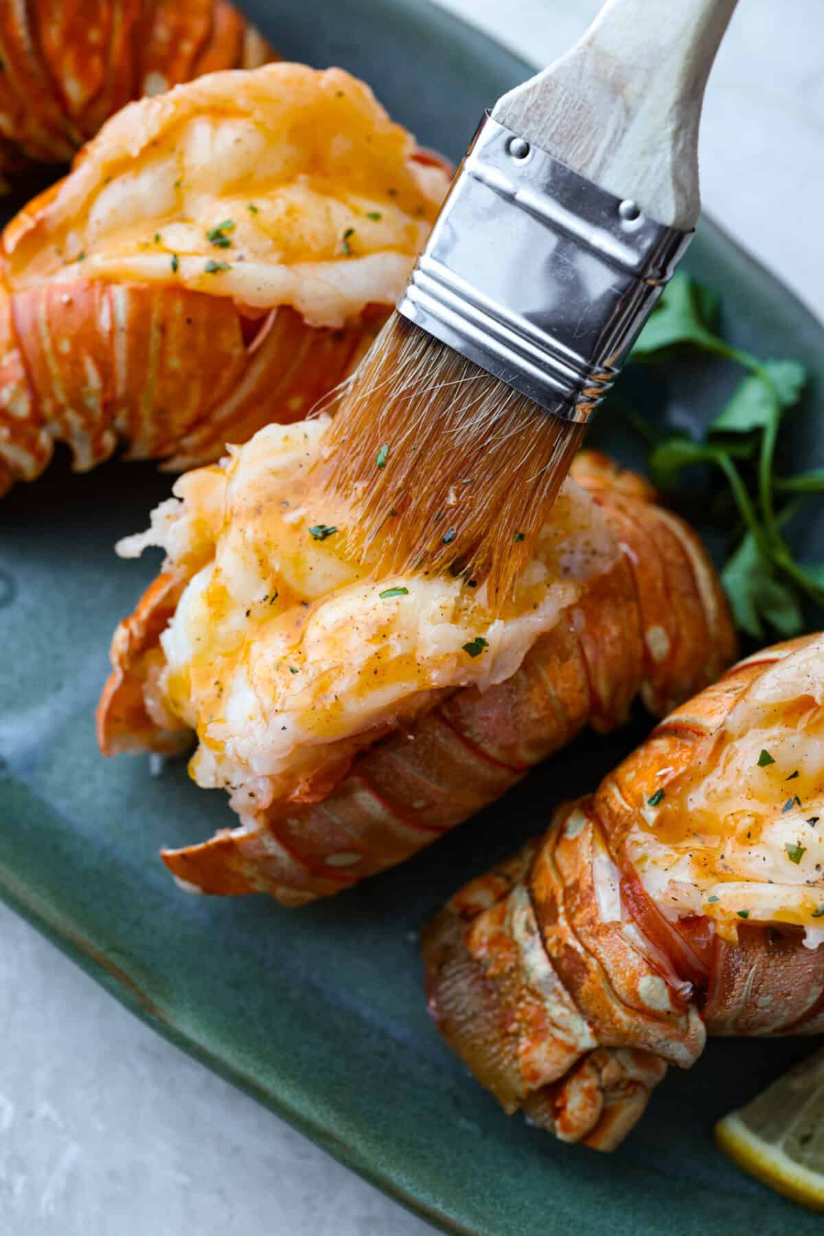 Instant pot lobster is the easiest way to bring a little luxury to your dinner table, no boiling pots or fancy techniques needed! In just minutes, the lobster cooks up tender, juicy, and perfectly steamed, ready to soak up a rich garlic herb butter. Someone spreading the herbed butter over the cooked tails.