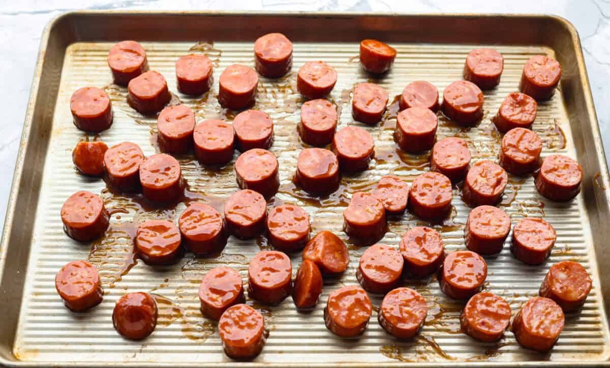 Overhead shot of glazed kielbasa slices spread out on a baking sheet. 