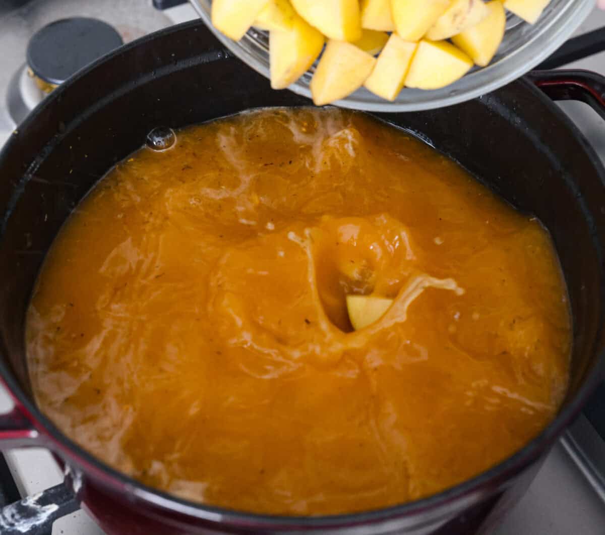 Overhead shot of someone pouring potatoes into the chicken broth onions and garlic.