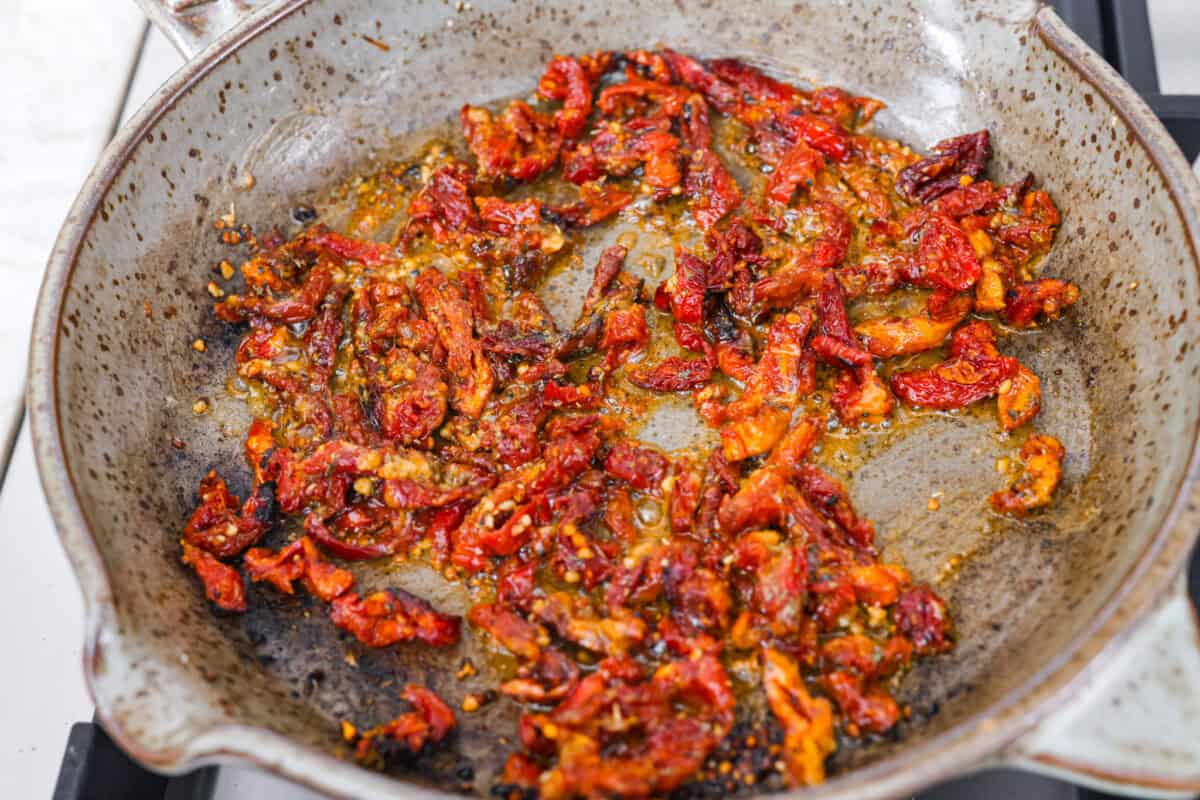 Overhead shot of sun-dried tomatoes and garlic with flour and seasonings added in the skillet. 