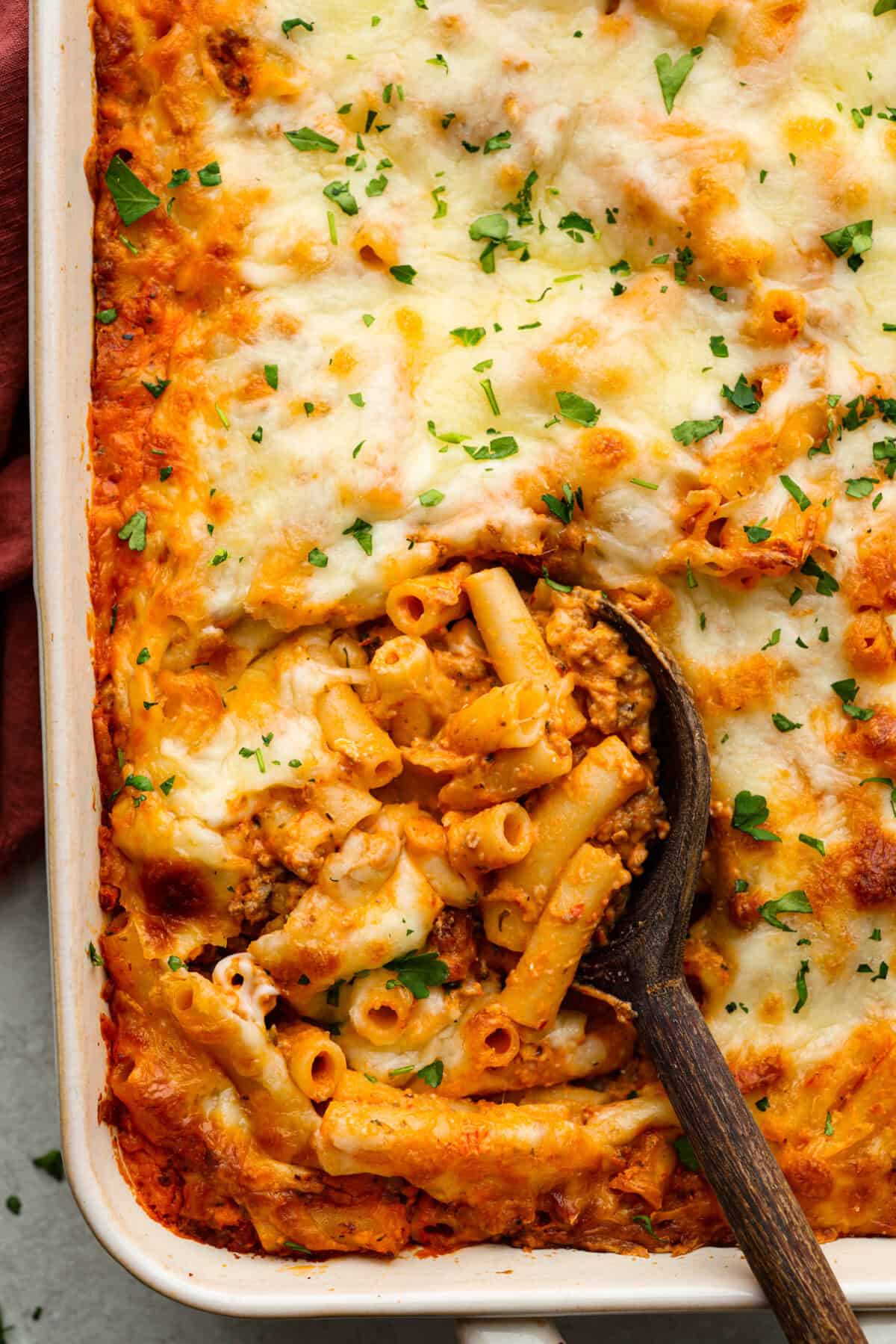 Overhead shot of million dollar baked ziti with a wooden serving spoon getting a scoop out. 