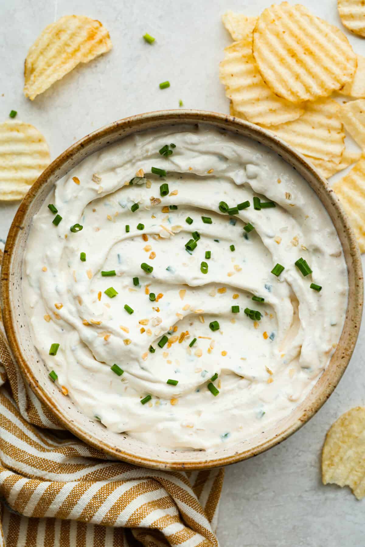 Overhead shot of sour cream and onion dip in a bowl with wavy chips around it. 