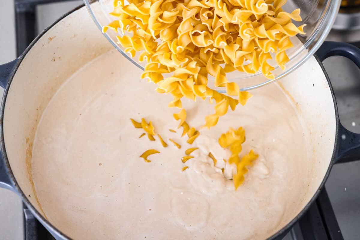 Angle shot of someone pouring noodles into the cream broth. 