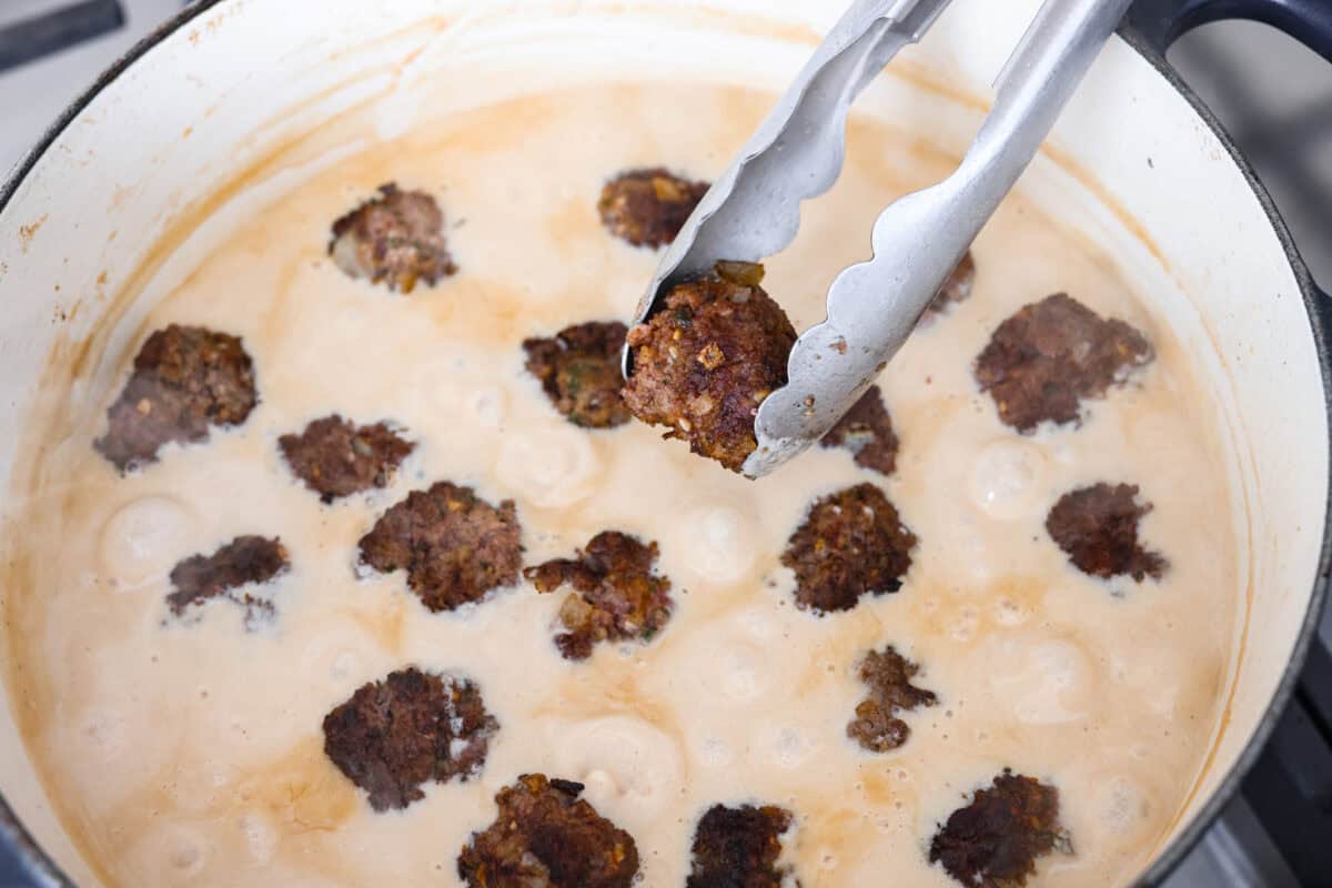 Overhead shot of someone placing the meatballs into the cream broth. 