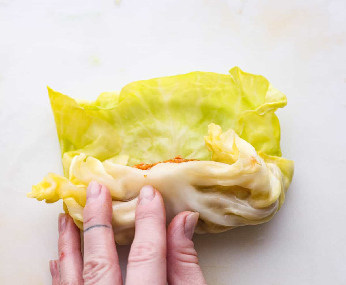 Close up shot of someone rolling up the filling in the cabbage leaf. 