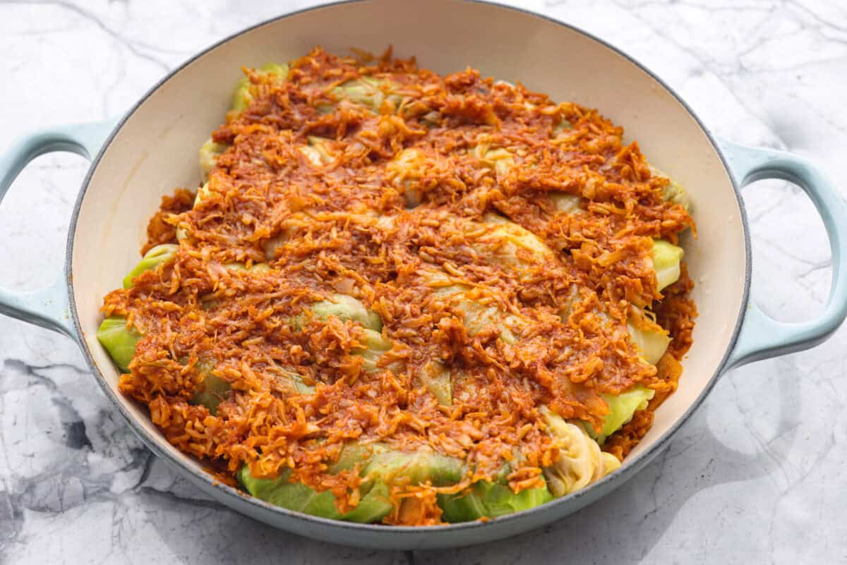 Angle shot of all of the filled cabbage leaves in the dutch oven covered in the sauerkraut mixture. 